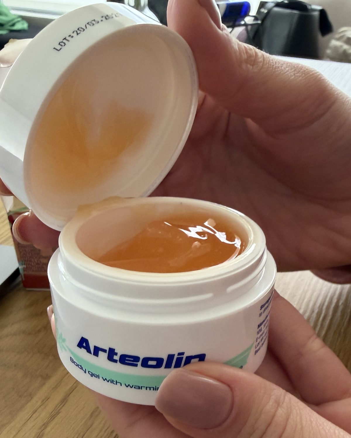 Kézben tartott, nyitott Arteolin tégely borostyánszínű, fényes géllel, mellette a felemelt kupak